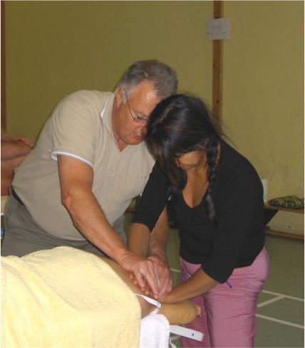 Två personer mobiliserar stel axelled på person liggandes på massagebänk.