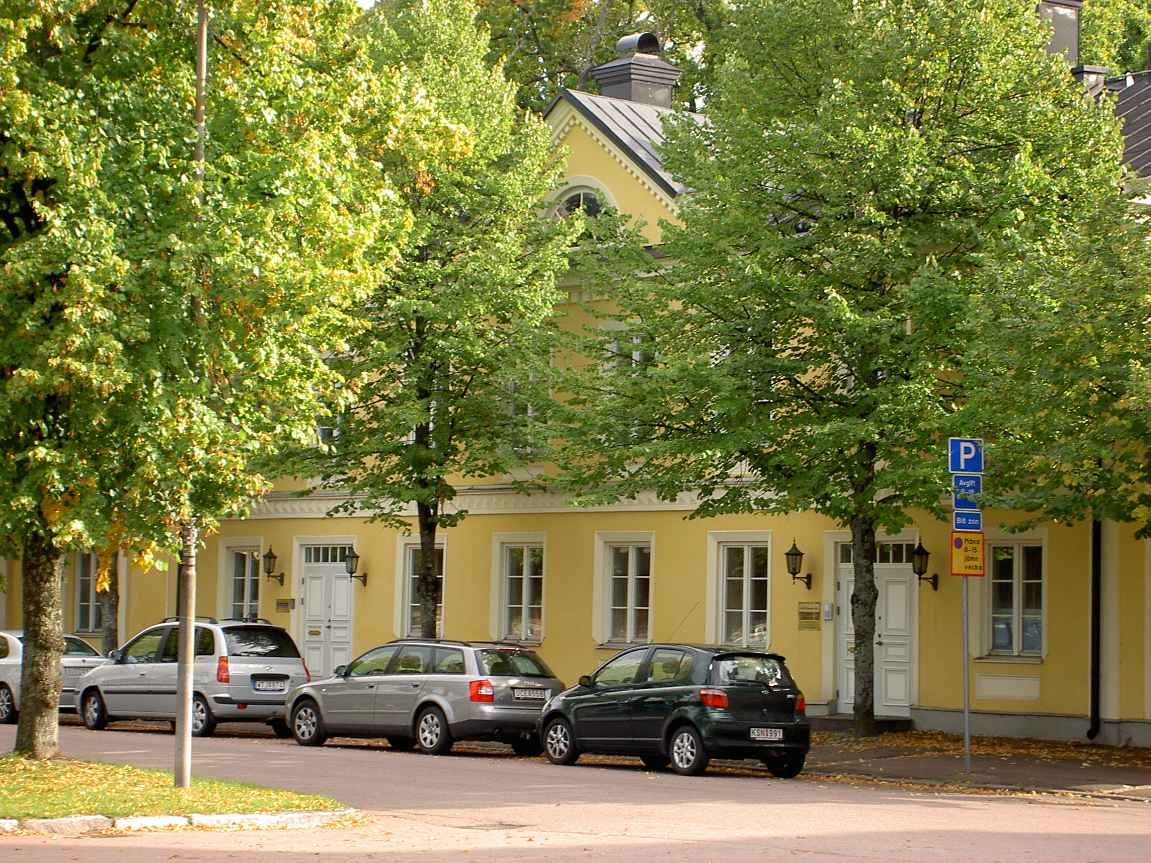 Entré till Ahlstrands Praktik, gult hus med gröna träd framför