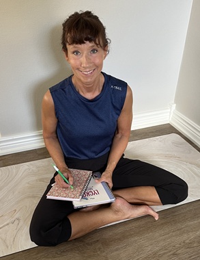 Malin Rask sitter i skräddarställning/korslagda ben med anteckningsböcker och en penna i händerna